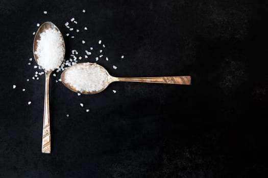 Salt crystals in old spoons on black background.
