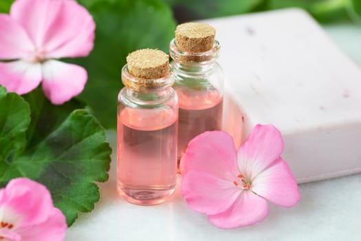 Plant extract in viles with geranium leaves and pink flowers and soap.