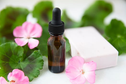 Plant extract in dropper bottle with geranium leaves,  pink flowers and soap.