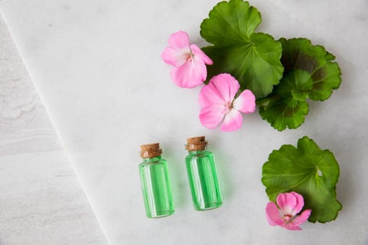 Plant extract in viles with geranium leaves and pink flowers, top view