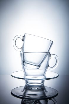 Two isolated transparent tea cups with saucers.