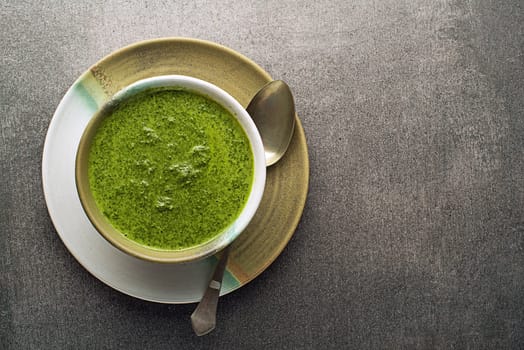 Spring healthy food. Green creamy soup with vegetables and herbs on gray background