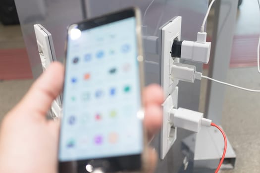 Female hands holding phone and using smartphone apps while charging it in a public place using electric plug and charging cable. Focus on charging adapter plugged in to free airport charging station.