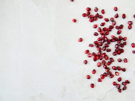 Flat lay pomegranate seeds on marble surface with copy space.