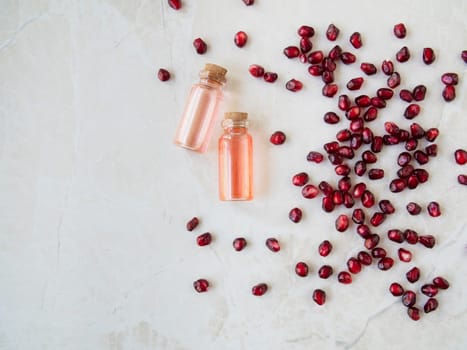Flat lay pomegranate seeds with small bottles of extract on marble surface with copy space.