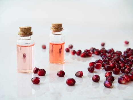 Two Small bottles of pomegranate extrace surrounded by pomegranate seeds.
