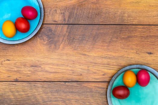 Six colorful Easter eggs on two plates in pastel colours on vintage oak background, top view