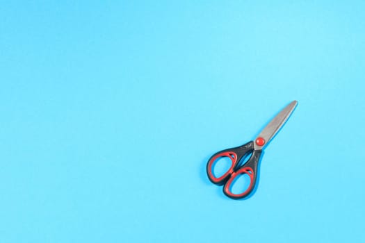 closed black scissors with red elements on blue background