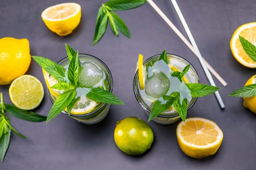 Top view of fresh lemonade with mint and ice in glasses on black background. Focus on leaf and ice.