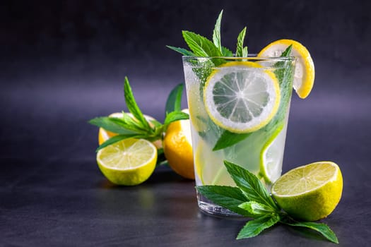 Cold refreshing summer lemonade with mint in a glass on a grey and black background. Focus on glass.
