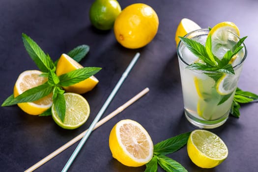 Cold refreshing summer lemonade with mint in a glass on a grey and black background. Focus on leaf in glass.