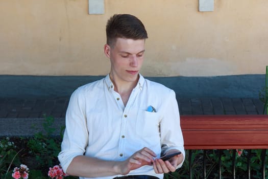 Outdoor portrait of modern young man with mobile phone in the bench