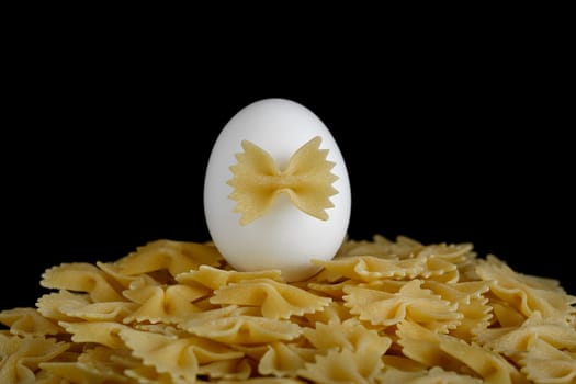 Pasta bows on a black background and a white egg on top, symbolizing the content of eggs in pasta