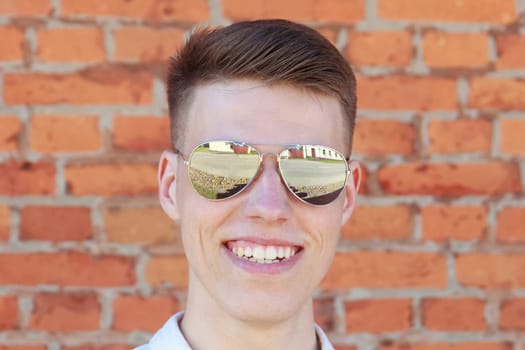 Smiling young man portrait with retro shiny drop sunglasses against brick wall