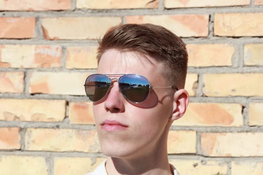Handsome cool young man with sunglasses against brick wall.Reflection of harbour in sunglasses.
