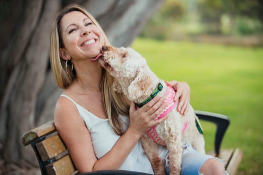 An aborable puppy is licking her owner's face as they relax together on a park bench.