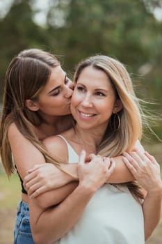 A teenage girl is hugging her mother from behind whilst kissing her on the cheek.