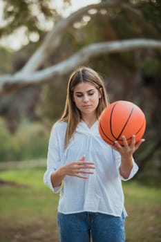 A teenage girl standing with a basketball outdoors.