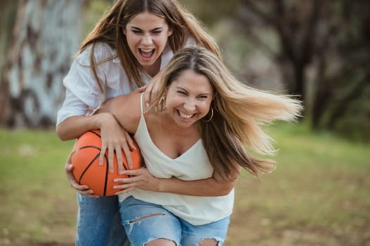 A teenage girl and her mother are playing basketball together outdoors.