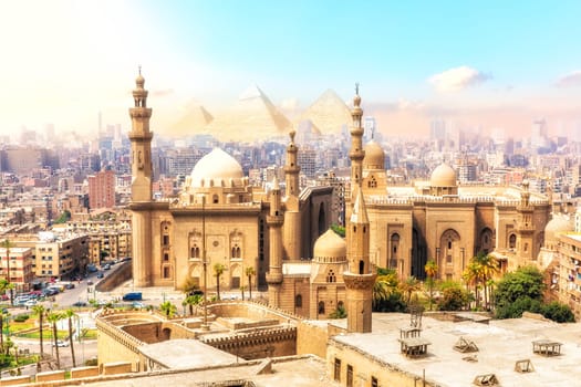 The Mosque-Madrassa of Sultan Hassan and the Pyramids on the background, beautiful view of Cairo, Egypt.