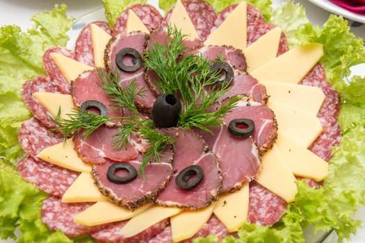 Sliced on a plate of sausage and cheese, decorated with greens and olives