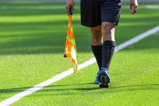 Football Assistant Referee walking with Flag on artificial turf.