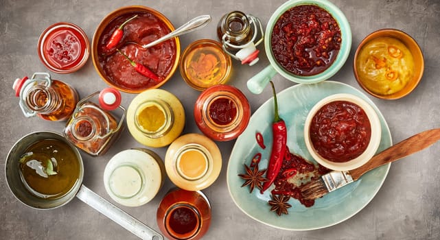 Overhead view of assorted savory, hot spicy and piquant sauces and marinades in bowls and bottles for a summer BBQ in a panorama banner