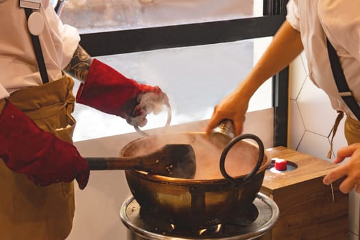 The hands of professional nougat manufacturers in the preparation of sweets in the copper kettle on an open flame. Selective focus on copper kettle. Malaga, Costa del Sol, Adalusia, Spain.