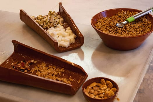 Various types of sweets made from nuts, white and brown nougat in brown bowls which have just been prepared fresh in nougat production and can be tasted by visitors. Selective focus on nougat.