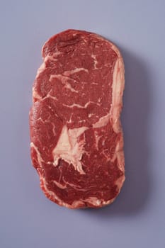 Thick succulent raw marbled rib eye beef steak on blue grey viewed from overhead ready for cooking on a summer picnic or BBQ