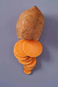 Sliced through raw fresh sweet potato or yam showing the bright orange flesh on a grey background viewed from above