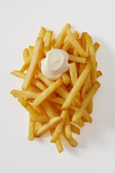 Tasty portion of golden fried potato chips , pommes frites or French fries with blob of mayonnaise or sour cream viewed top down on white