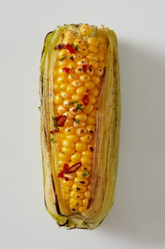Fresh spicy grilled corn on the cob seasoned with red chili pepper in a close up view with outer leaves on white