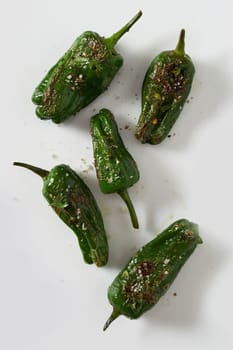Grilled or roasted spicy seasoned whole green Jalopeno chili peppers scattered on white viewed from above