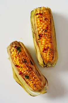 Spicy grilled corn on the cob seasoned with chili from a summer barbecue viewed from above on white in a healthy diet and seasonal cuisine concept