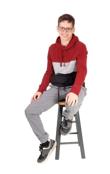 A lovely young teenager boy sitting in the studio in a nice sweater .wearing glasses and smiling friendly, isolated for white background.