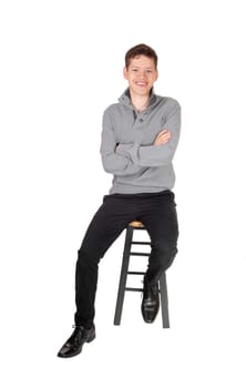 A young teen boy, sitting in a gray sweater with his arms crossed smiling.on a chair, isolated for white background.