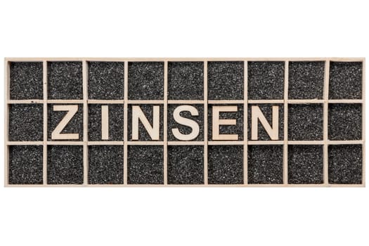 Plywood letters arranged in a collecting box with black decorative sand representing the word ZINSEN in top view isolated on white.
