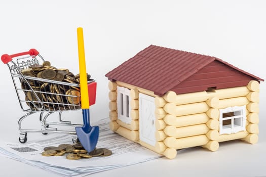 A trolley with money in the bills for an apartment, a shovel stands next to it, a toy house is near