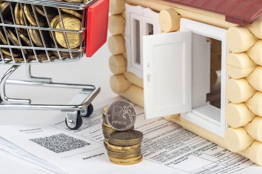 A cart with money, a stack of money and a coin of one ruble in the bills for an apartment, in front of the door to the house