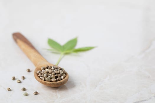 Cannabis seeds in a wooden spoon with leaf in the background on a marble surface with copy space.