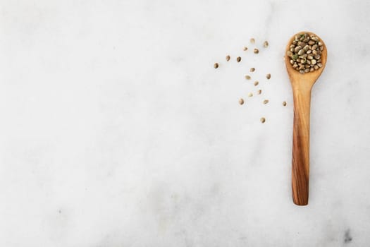 Cannabis seeds in a wooden spooon on a light marble surface with copy space, viewed from directly above.