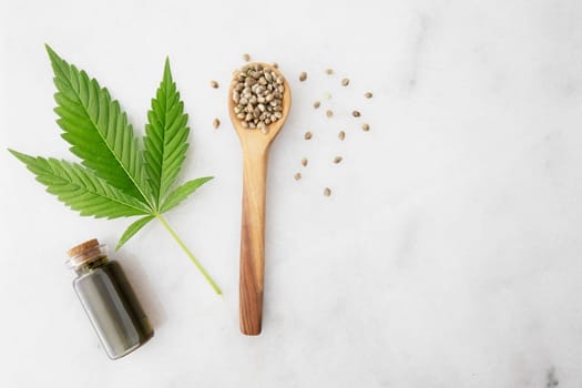 Small bottle of CBD oil with cannabis leaf and seeds in a wooden spoon, viewed from directly above.