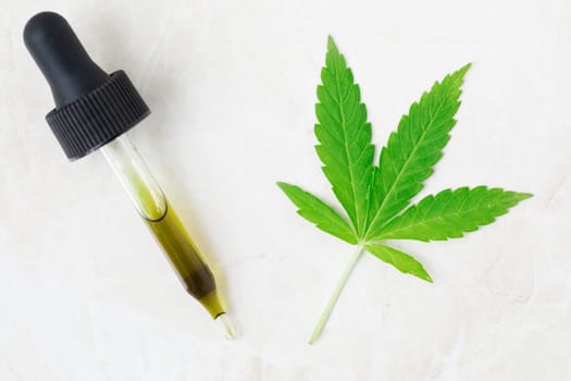 Dropper full of CBD oil and cannabis leaf viewed from above.
