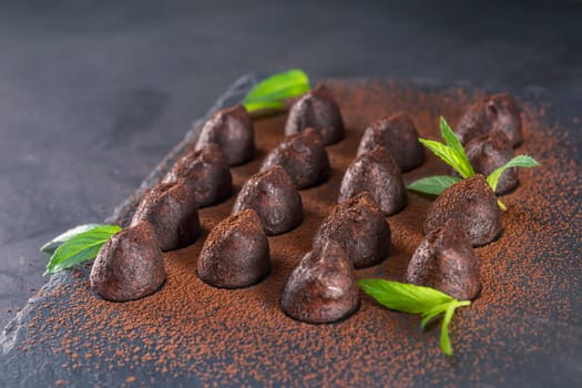 Homemade chocolate truffles with mint sprinkled with cocoa powder on slate. Focus on second truffle in road.