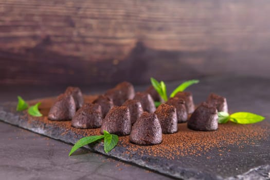 Homemade chocolate truffles with mint sprinkled with cocoa powder on slate. Focus on first truffle.