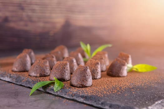 Homemade chocolate truffles with mint sprinkled with cocoa powder on slate. Focus on first truffle