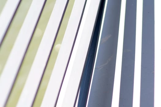 The close-up of the white-painted crossbars of a bridge railing, which casts symmetrical shadows.