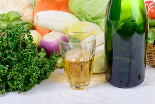 Glass and bottle of cider with vegetables on table