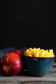 Chopped nectarines in bowl with whole nectarine on ths side, low key lighitng and vertical orientation.